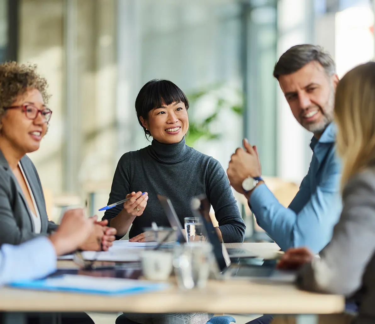 Healthcare workers in a meeting around a board room table utilizing the team meeting feature in the Kipu compliance software